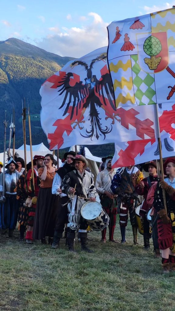 Mitglieder des Rotwelschen Haufens in historischer Gewandung mit Fahnen vor einer Berglandschaft